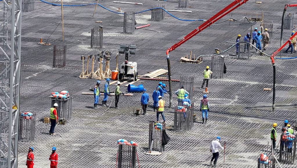Rozległy kosz zbrojeniowy płyty fundamentowej widziany z góry, robotnicy w kaskach rozprowadzają beton z wysięgnika pompy